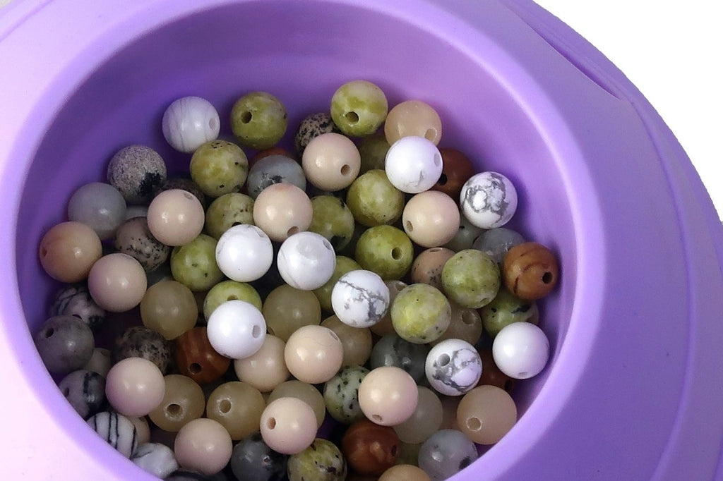Close-up of a pile of multicolor natural stone beads in a purple container, showing various colors and patterns.