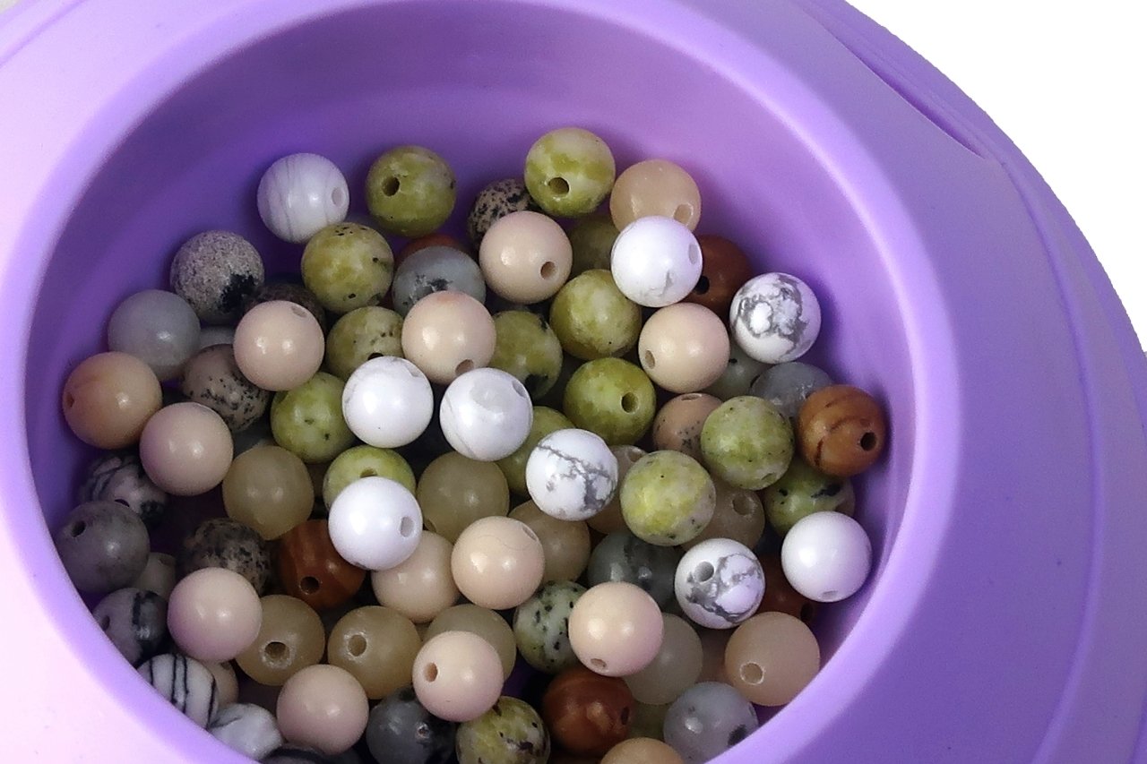 Close-up of a pile of multicolor natural stone beads in a purple container, showing various colors and patterns.