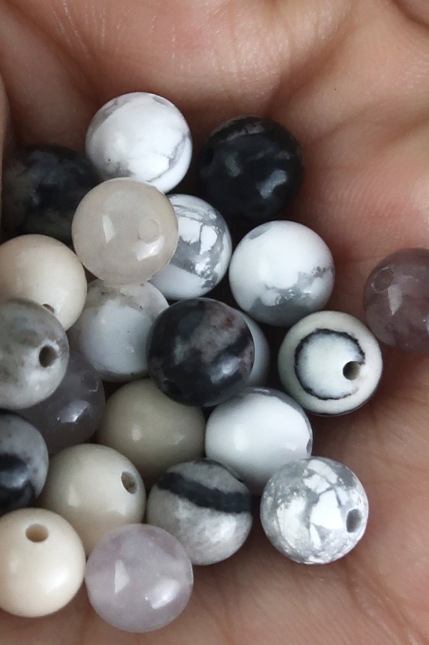Hand holding a collection of natural round stone beads in various colors including white, black, grey, and purple.