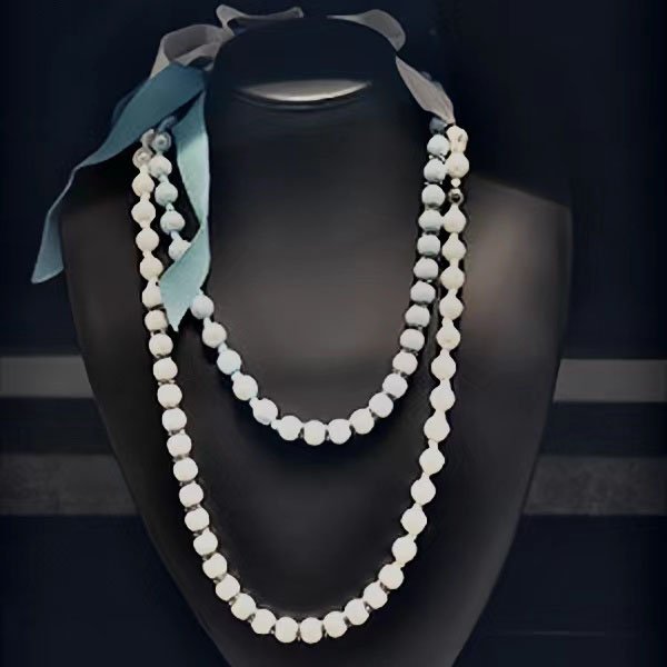 Two strands of white gemstone beads draped on a black mannequin bust with blue and gray ribbons tied at the top.