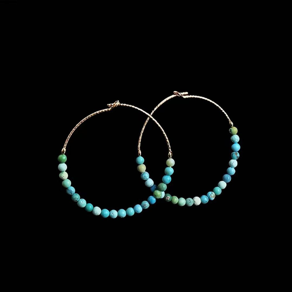 Pair of gold hoop earrings with multicolor turquoise-like beads against a black background