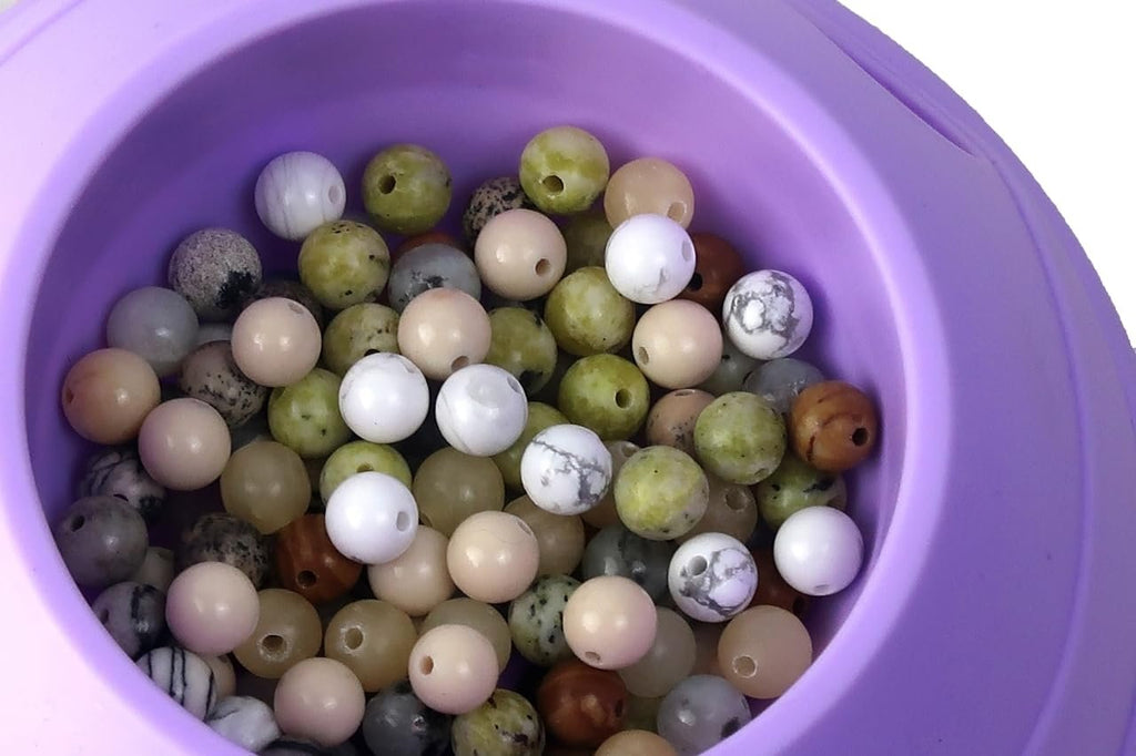 Close-up of multicolor natural stone beads in a purple container, showing various patterns and colors.