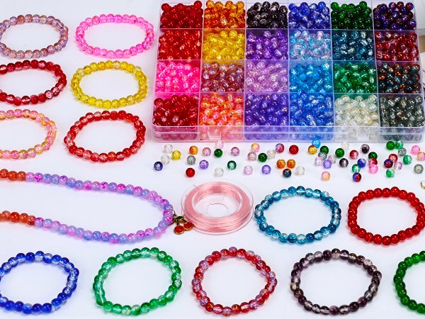 Assorted colorful glass beads and finished bracelets arranged on a white surface, with a spool of pink thread.