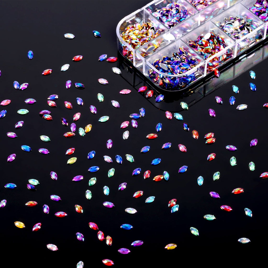 Flat back acrylic horse eye nail rhinestones in rainbow colors scattered on a black surface next to an organized storage box.