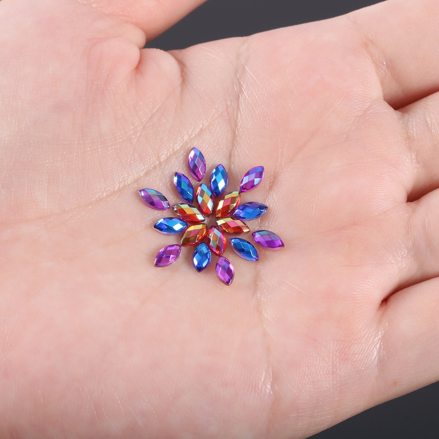 Hand holding a cluster of colorful horse eye nail rhinestones arranged in a flower shape.