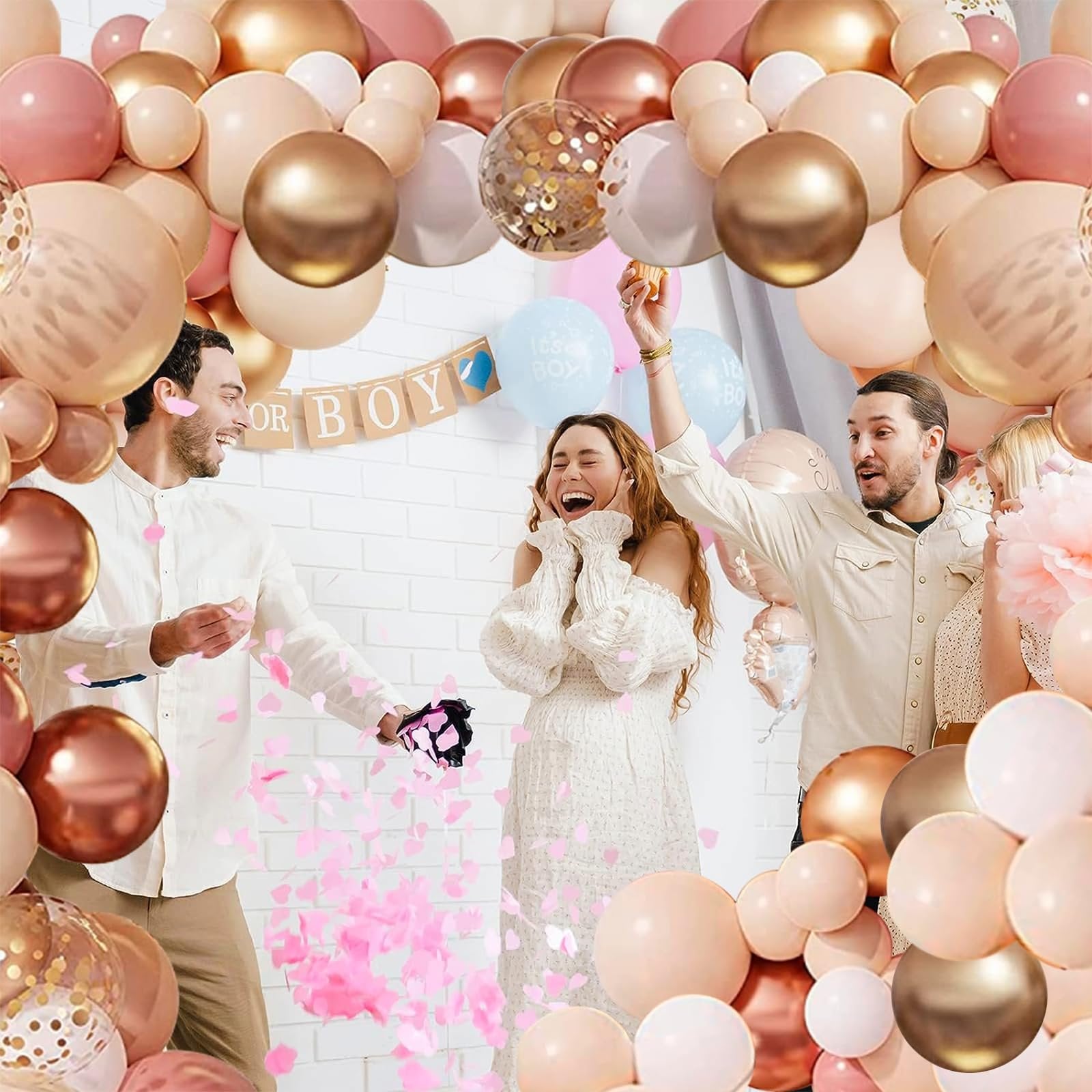 People celebrating a gender reveal with a balloon garland and confetti, with 'OR BOY' banner in background.