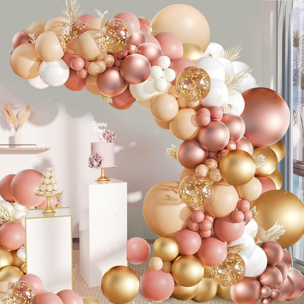 Balloon garland arch in blush, rose gold, and gold tones with confetti balloons, set against a backdrop with a cake and dessert stand.