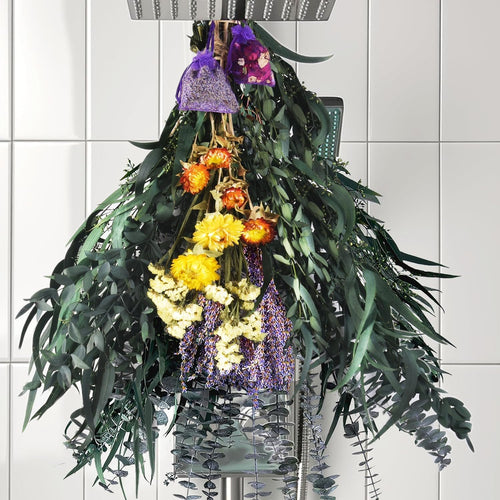 Dried eucalyptus and lavender bouquet hanging from a shower head with small sachets.