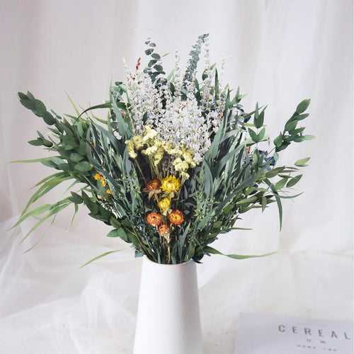 Dried eucalyptus and lavender bouquet in a white vase with a magazine on the side
