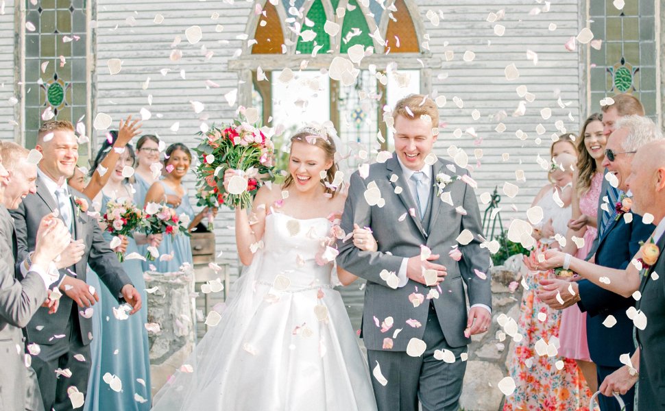 Newlyweds walking through falling dried flower petals with wedding guests watching and throwing petals.