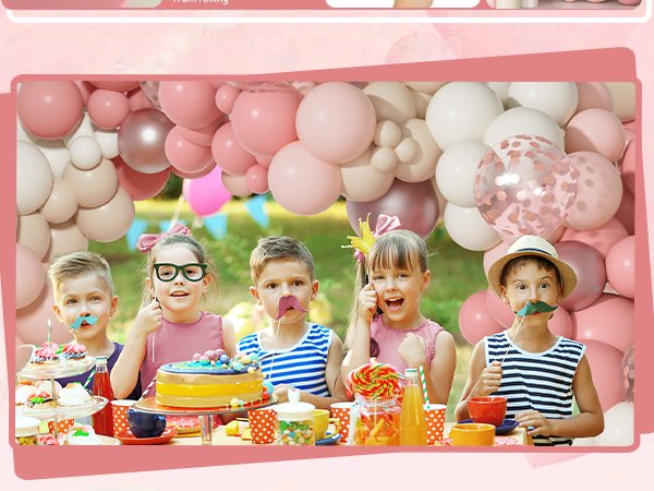 Children with party props in front of a dusty pink balloon arch garland at a table with cake and treats