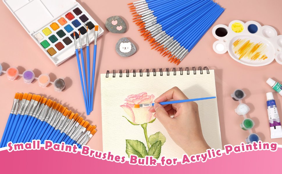 Flat lay of art supplies including paint brushes, watercolor palette, paints, and a person painting a rose on a sketchbook.