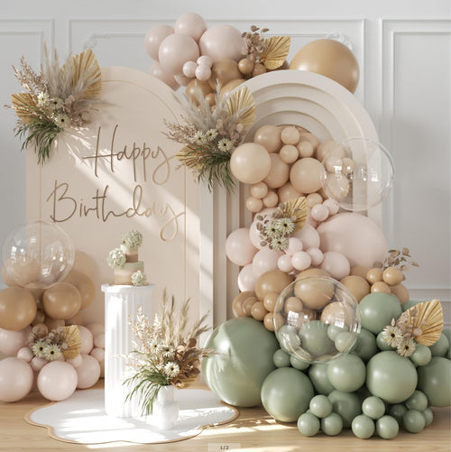 Balloon arch with sage green, dusty green, tan, and nude balloons, featuring a 'Happy Birthday' cutout and a tiered cake.