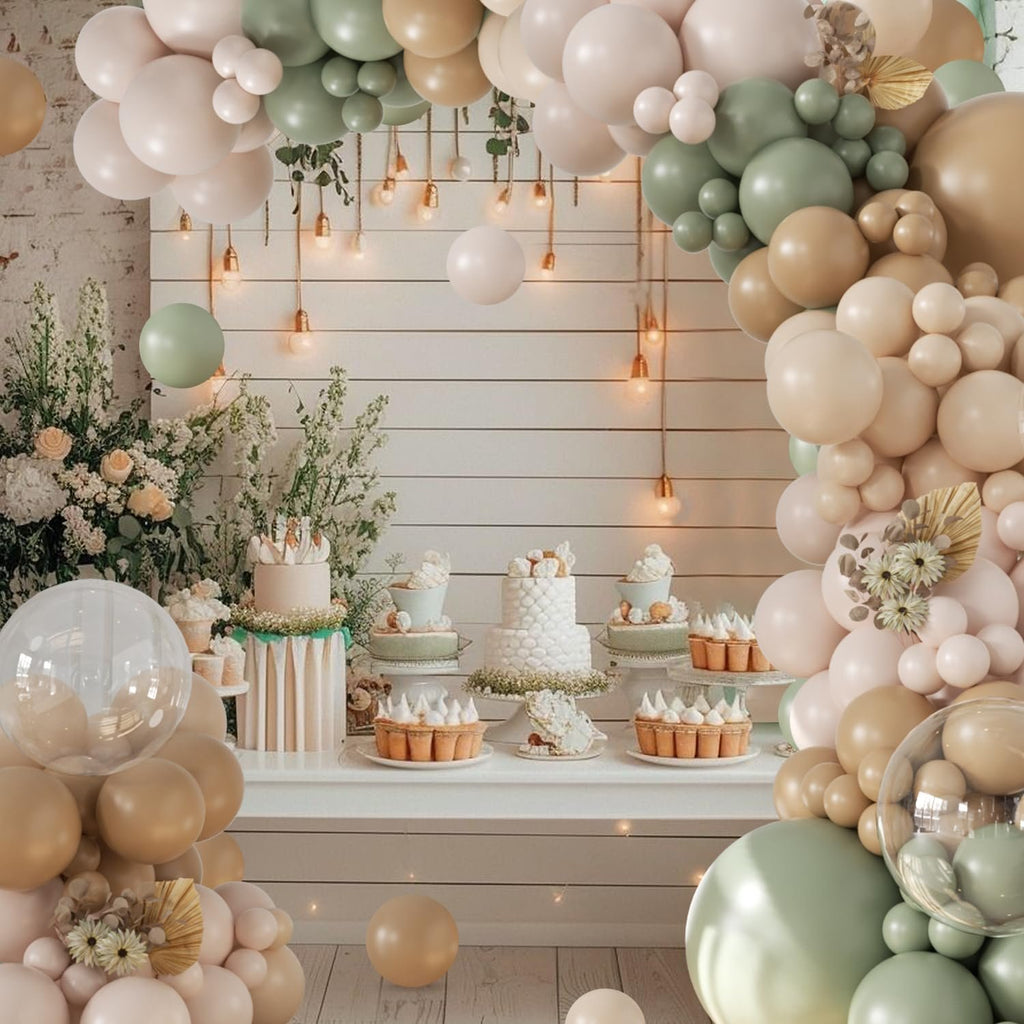 Sage green and neutral balloon arch over a dessert table with cakes and tarts, decorated with flowers and string lights.
