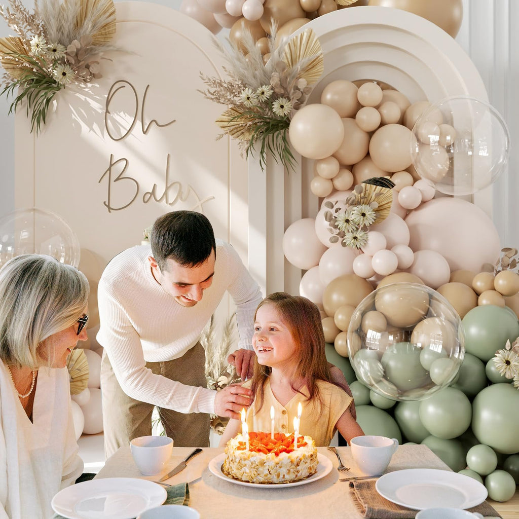 Family celebrating a birthday with a cake and balloons, featuring a sage green balloon arch.