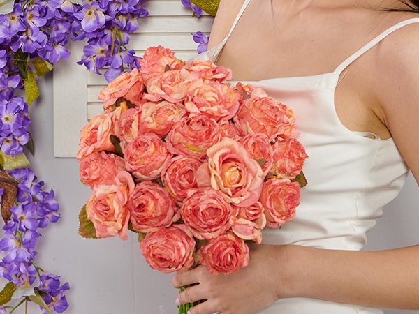 Woman holding a bouquet of pink artificial roses with purple wisteria vines on the left.