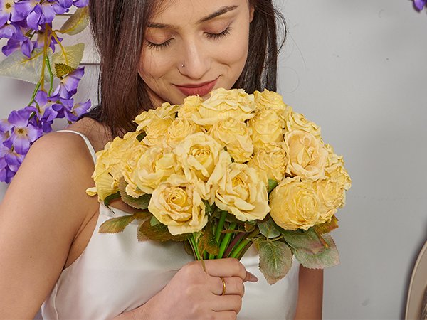 Woman holding a bouquet of yellow artificial roses with purple flowers in the background