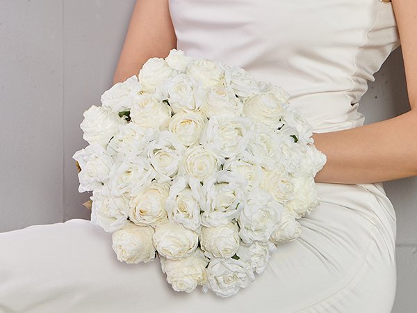 Woman in a white dress holding a large bouquet of white artificial roses.