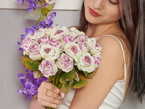 Woman holding a bouquet of artificial pink and white roses with purple flowers and green leaves.