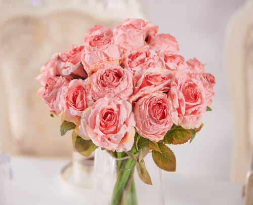 Bouquet of 12 pink artificial roses in a clear glass vase, with green stems and leaves.