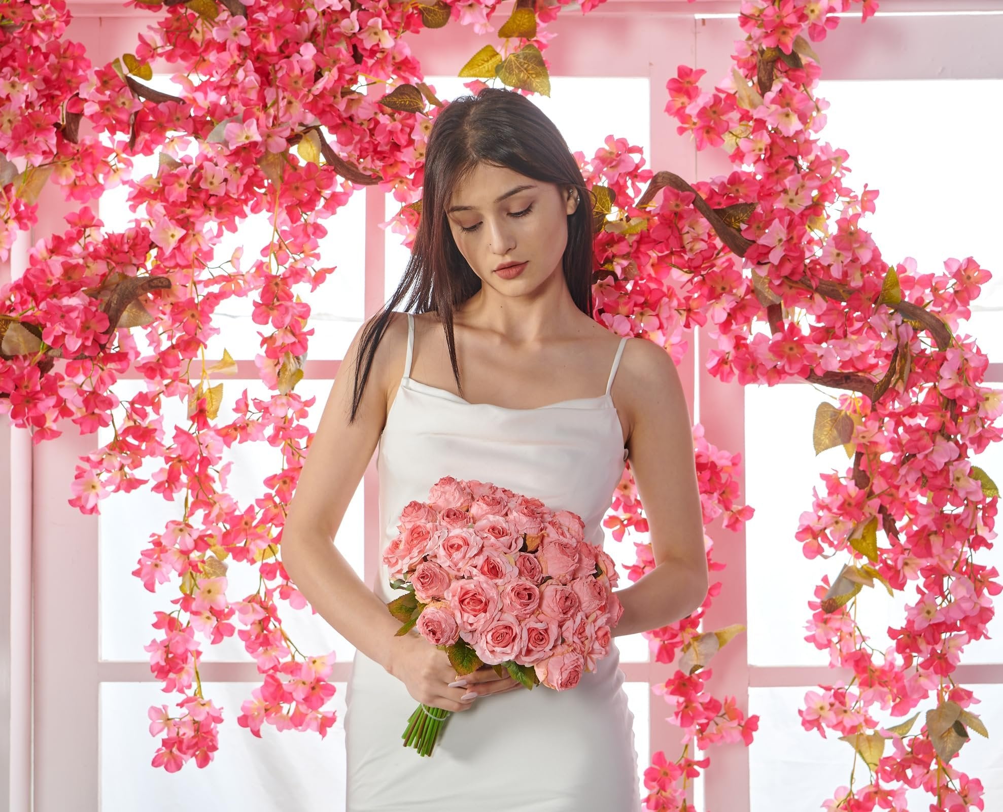 Woman in white dress holding a bouquet of pink artificial roses, surrounded by pink floral branches.
