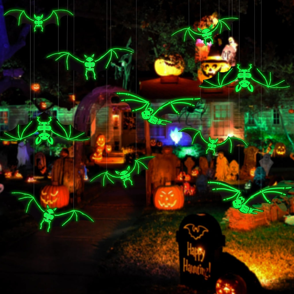 Glowing skeleton bats hanging as Halloween decorations in a yard with pumpkins and a tombstone.