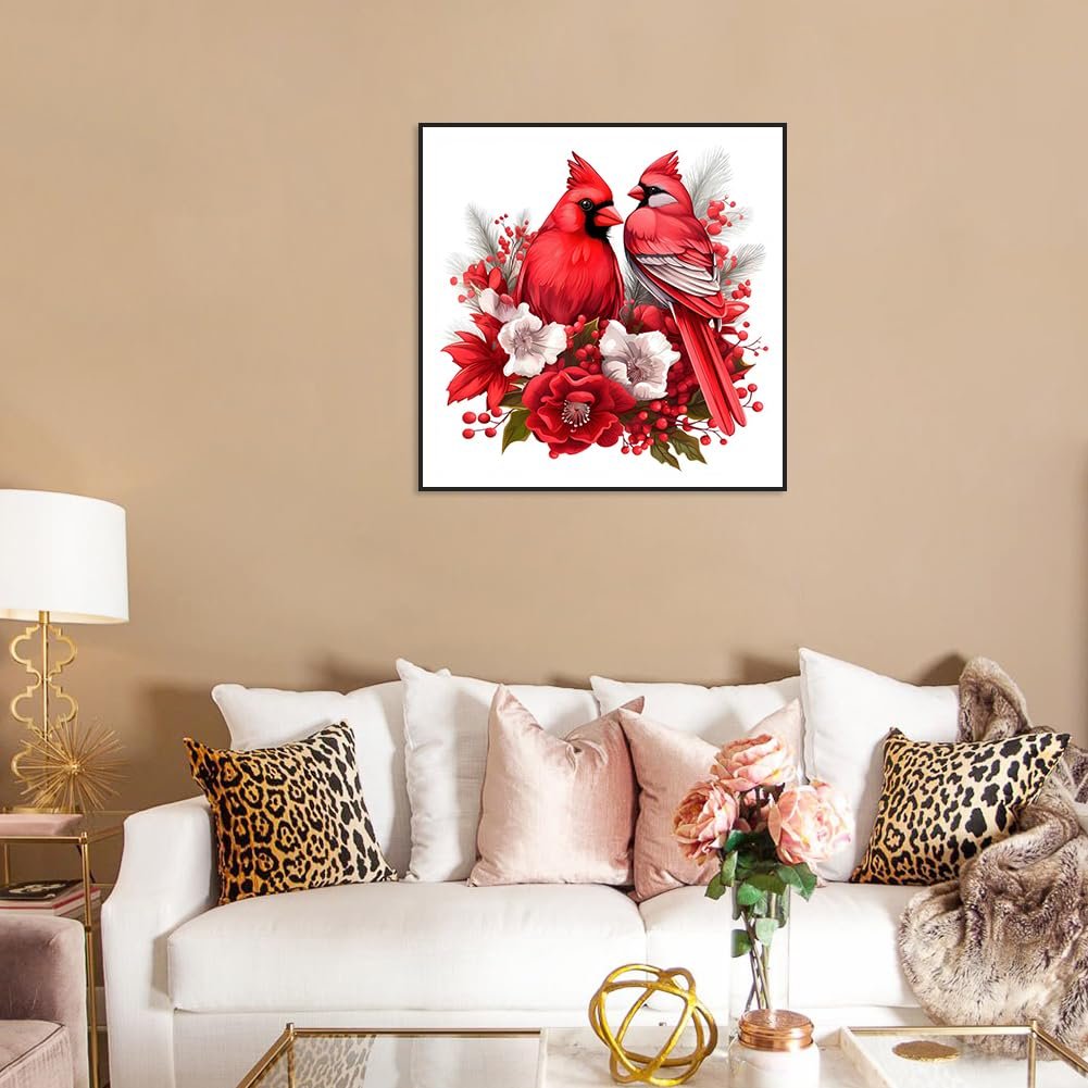 Two red cardinals perched on a floral arrangement, framed and hanging on a wall above a sofa.