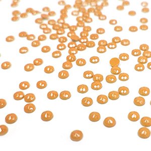 Scattered round orange diamond painting beads on a white surface, close-up shot with shallow depth of field.