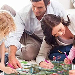 Family working on a 5D diamond painting kit with a bird landscape design on the floor.