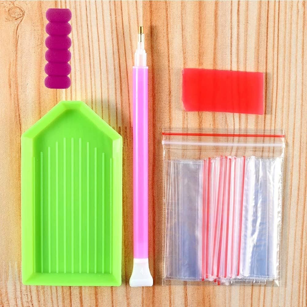 Diamond painting kit tools including a pink drill pen, green tray, purple grip, red sticky wax, and small plastic bags on a wooden background.