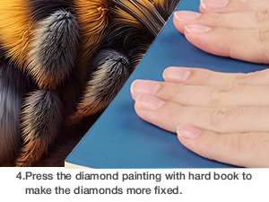 Close-up of bee and sunflower diamond painting kit with hands pressing down on canvas with a book.