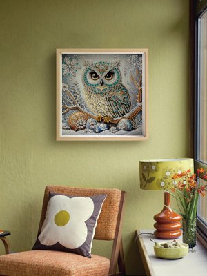 Framed 5D diamond art painting of a snowy owl perched on a branch, displayed on a wall above a chair.