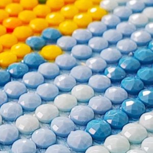 Close-up of colorful diamond art painting beads in rows, showing yellow, orange, light blue, and white beads.