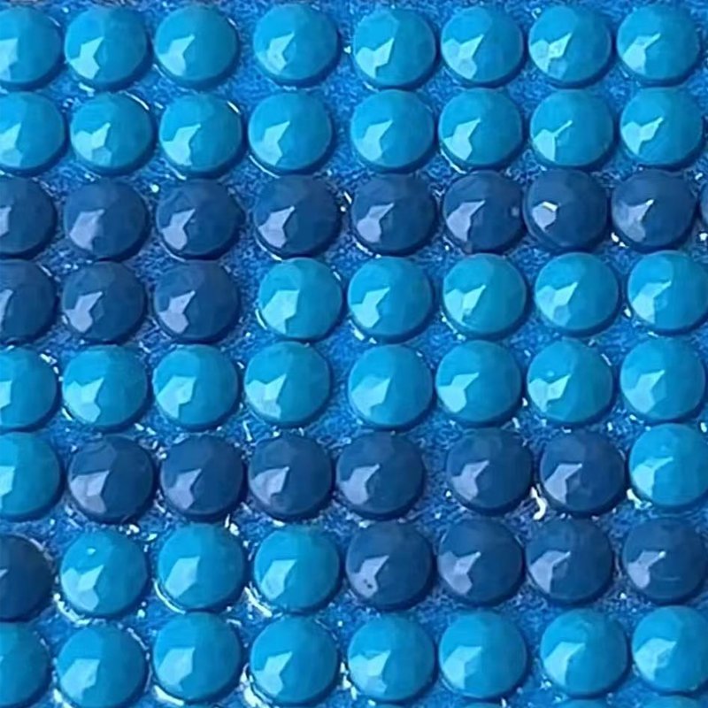 Close-up of a diamond art kit canvas showing rows of round blue resin gems adhered to a blue background.