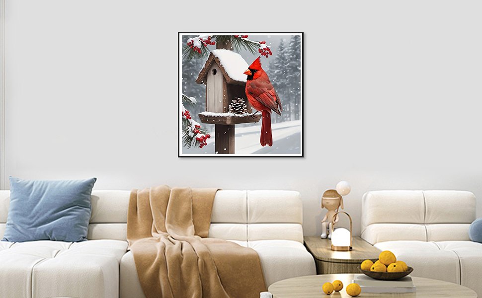 Framed diamond painting of a cardinal on a birdhouse in a snowy forest setting, displayed on a wall above a sofa.