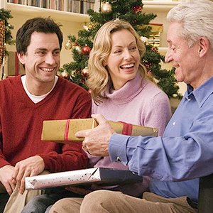 Family exchanging Christmas gifts in front of a decorated tree, smiling and laughing.