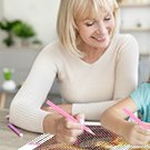 Woman and child doing a diamond painting kit together at a table, using pink diamond pens.