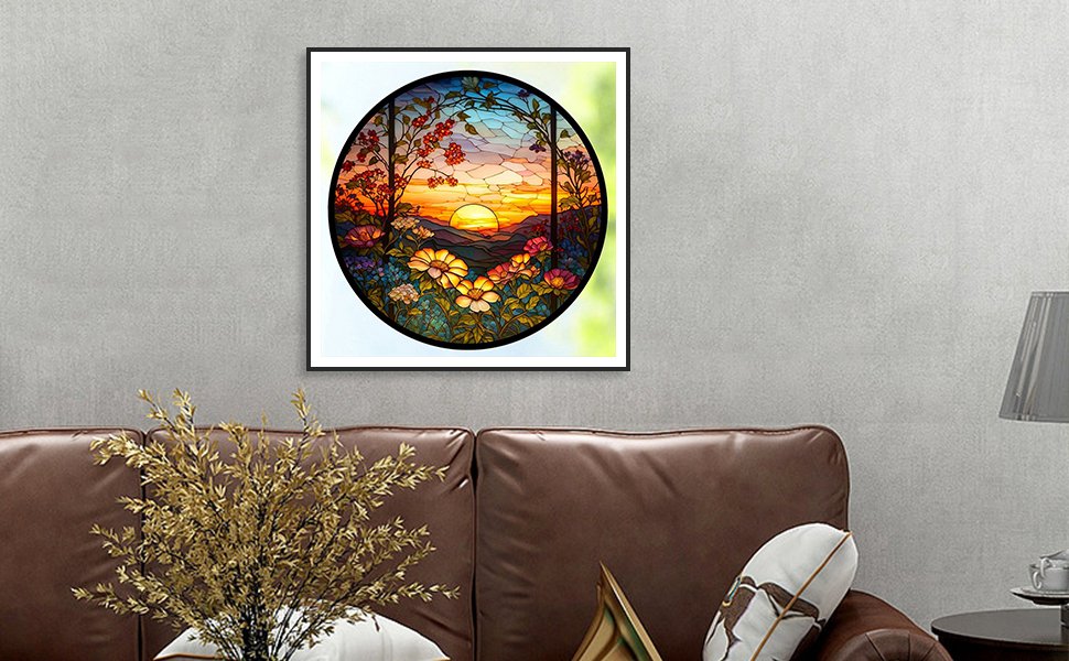 Framed stained glass art of a sunset over mountains with flowers in the foreground, displayed on a wall above a sofa.