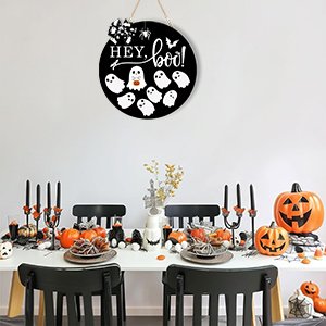 Round Halloween door sign with ghosts and 'Hey, boo!' text hanging above a decorated dining table.