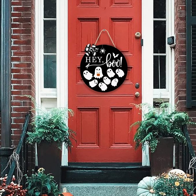 Round black Halloween door sign with ghosts and 'Hey Boo' text hanging on a red front door.
