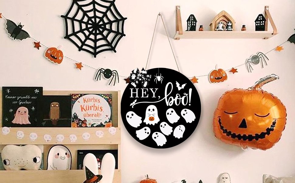 Round black Halloween door sign with 'Hey Boo!' text and ghost graphics, hanging on a wall with decorations.