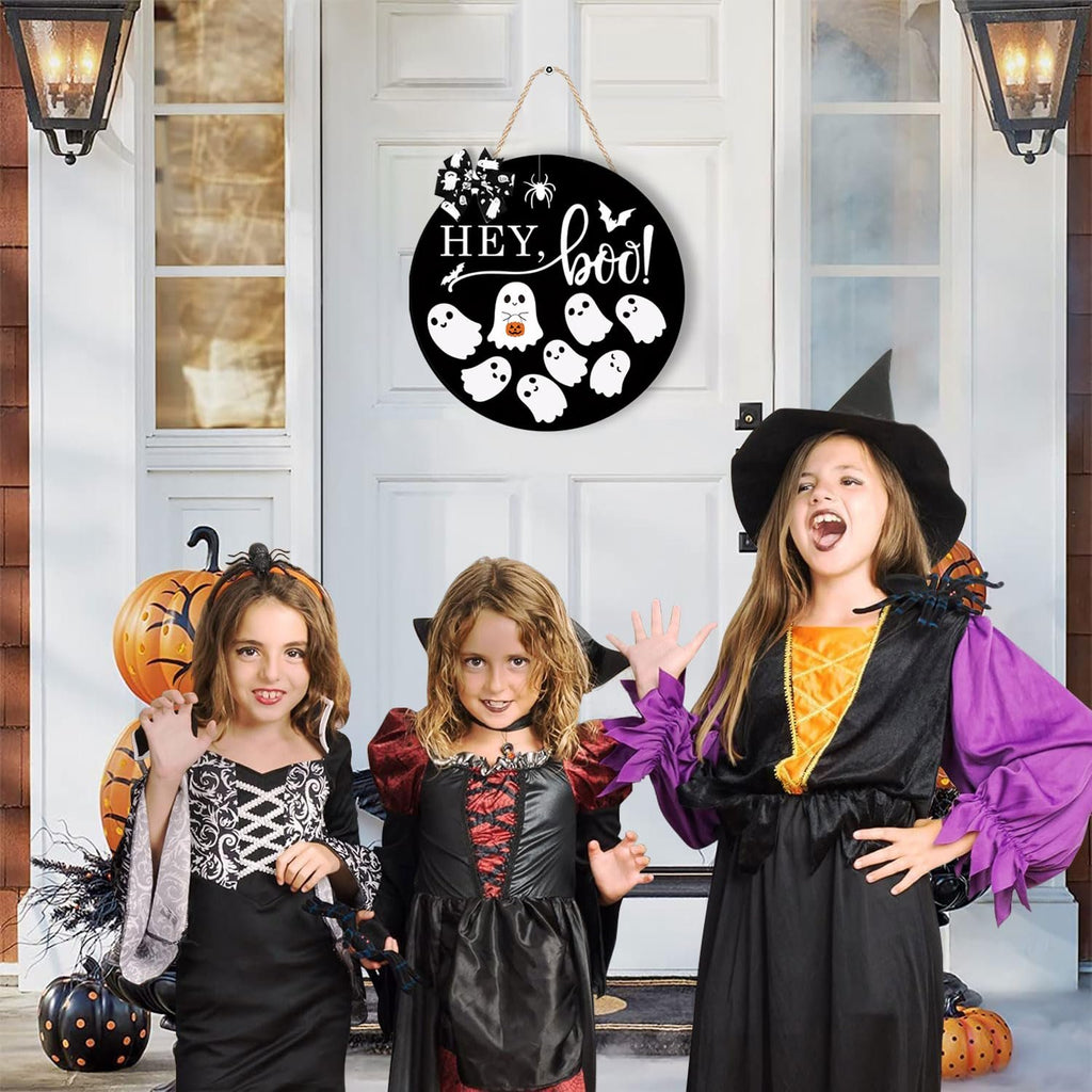Three children in Halloween costumes posing in front of a door with a round wooden Halloween sign