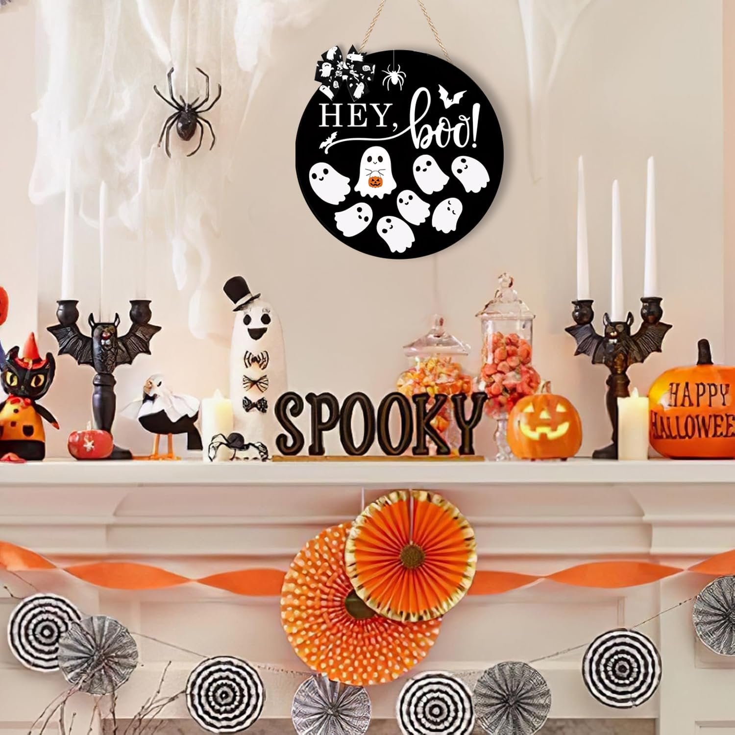Round black Halloween door sign with white ghosts and text 'Hey, Boo!' hanging above a decorated mantelpiece.