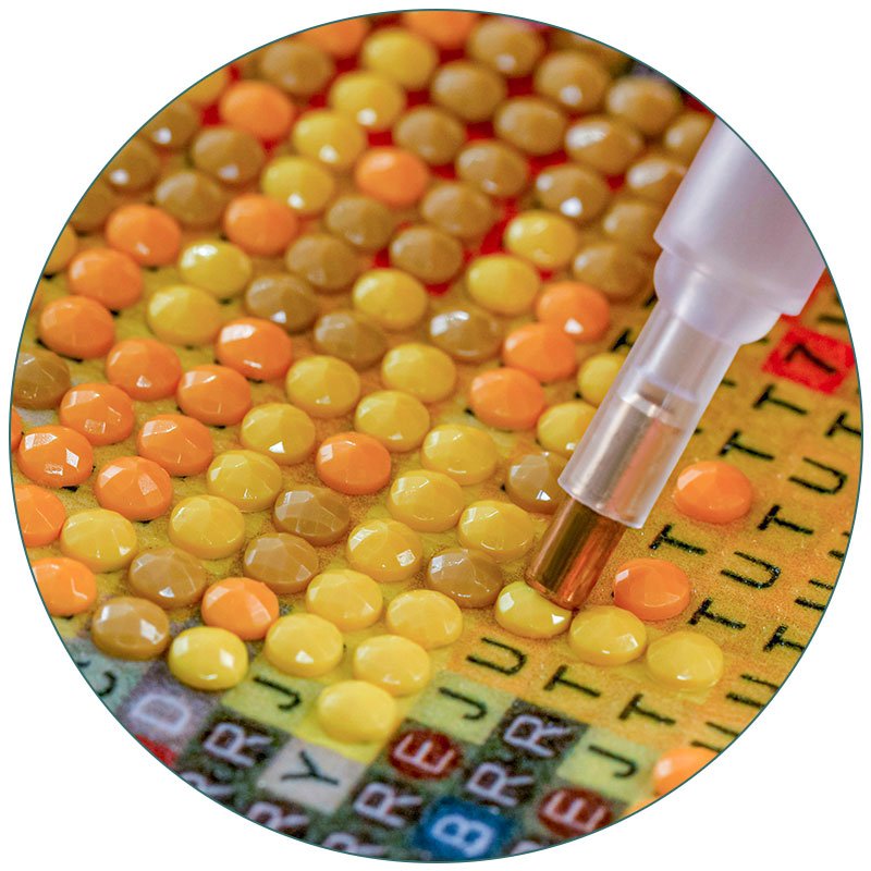 Diamond painting kit with tool placing a yellow crystal onto a canvas with printed letters and numbers.