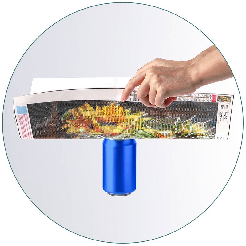 Diamond painting canvas with sunflower design, held by a hand over a blue can