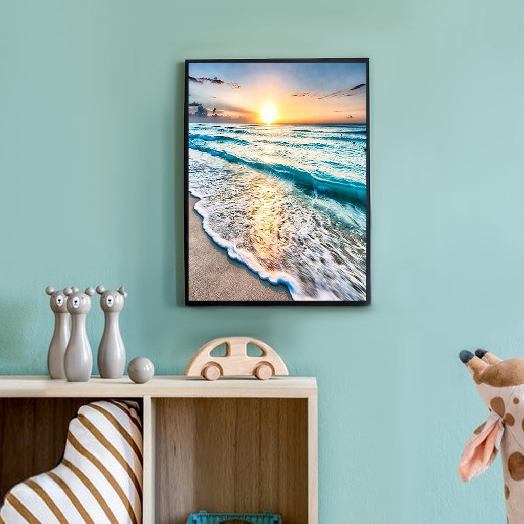 Framed diamond painting of a serene beach sunset with waves crashing on the shore, displayed on a wall above a shelf with toys.