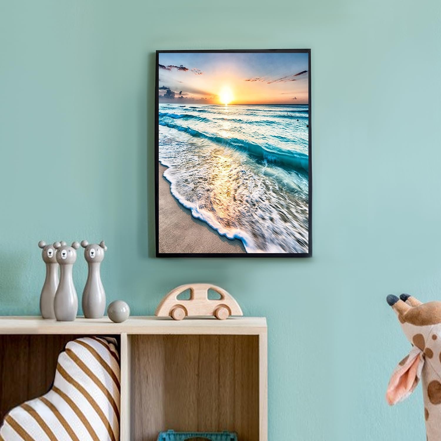 Framed diamond painting of a serene beach sunset with waves crashing on the shore, displayed on a wall above a shelf with toys.