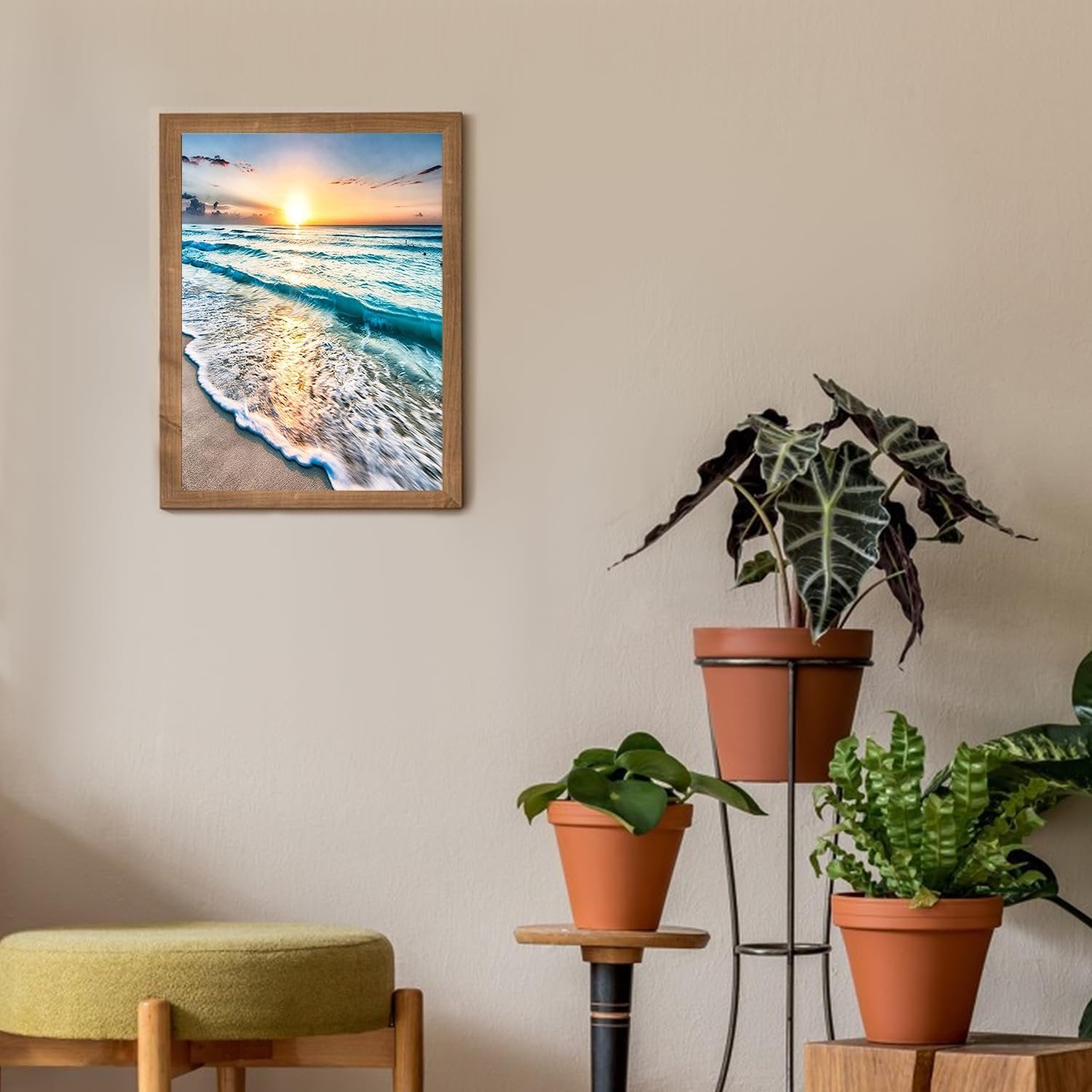 Framed diamond painting of a serene beach sunset with waves crashing on the shore, displayed on a wall above plants and a stool.