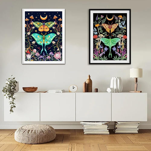 Two framed diamond art paintings of luna moths, mushrooms, and celestial elements displayed on a wall above a credenza.