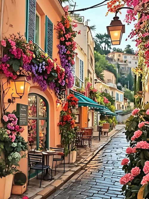 Charming European street scene with buildings adorned with abundant flowers, cobblestone street, and outdoor cafe seating.